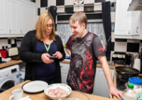 Carer supporting a young adult in preparing food in the kitchen