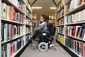 Young person in an electric wheelchair selecting books at a library