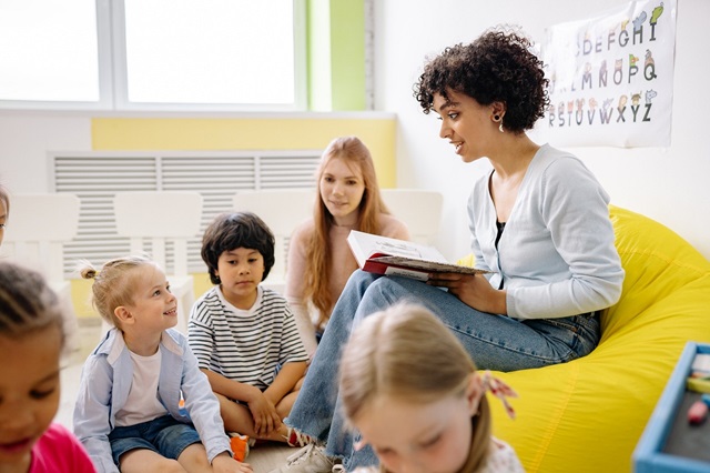 A childminder sitting on a bean sack reading to young children.