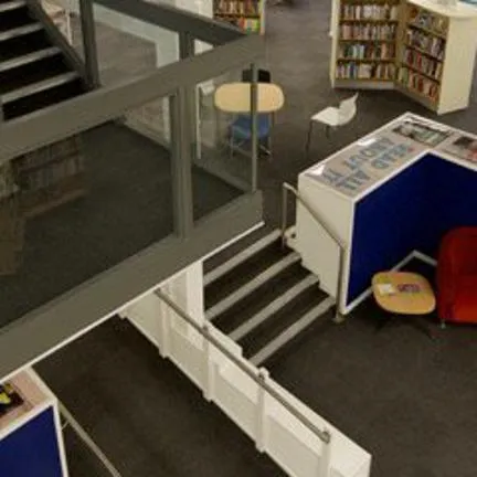 Inside of Arnold library from a mezzanine, showing stairs, shelves with books and cosy chairs.